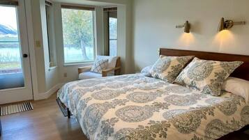 A bedroom with a large bed, two windows, a chair, and a door.