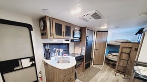 Une cuisine compacte pour camping-car, équipée d’un évier, d’une cuisinière et d’une machine à café.