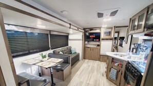 Un intérieur de camping-car compact comprenant un coin cuisine, un espace salon avec une table et un téléviseur fixé au mur.