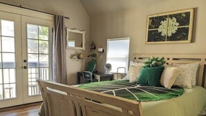 A bedroom with a wooden bed, a desk with a chair, a window with blinds, and a door with a curtain. - Green Grove at Captain's Cove, located in the heart of Old Colorado City 2 (Colorado Springs)