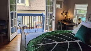 A bedroom with a bed, a desk with a lamp, and a balcony with chairs. - Green Grove at Captain's Cove, located in the heart of Old Colorado City 2 (Colorado Springs)