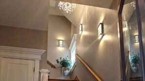 Una escalera de madera con barandilla blanca, una puerta blanca a la izquierda y una lámpara fijada a la pared.