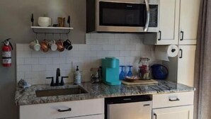Una cocina compacta con armarios blancos, un microondas integrado, lavavajillas y una encimera con distintos utensilios de cocina.