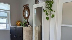 Una habitación con un aparador negro, una puerta blanca con paneles de vidrio esmerilado, un espejo y una planta.