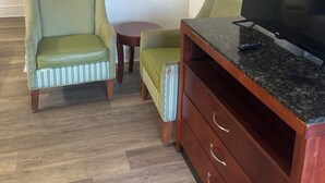 Una habitación con televisión sobre una encimera de mármol, un sillón verde, un sillón a rayas y una pequeña mesa de madera.