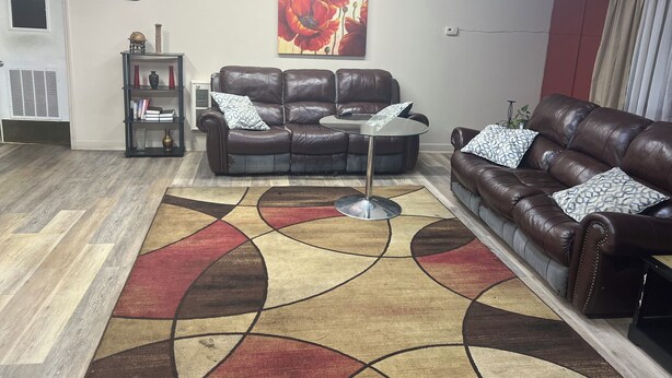 Un salón con dos sofás de cuero marrón, una mesa de centro de vidrio, una alfombra estampada, un reloj de pared y un cuadro.