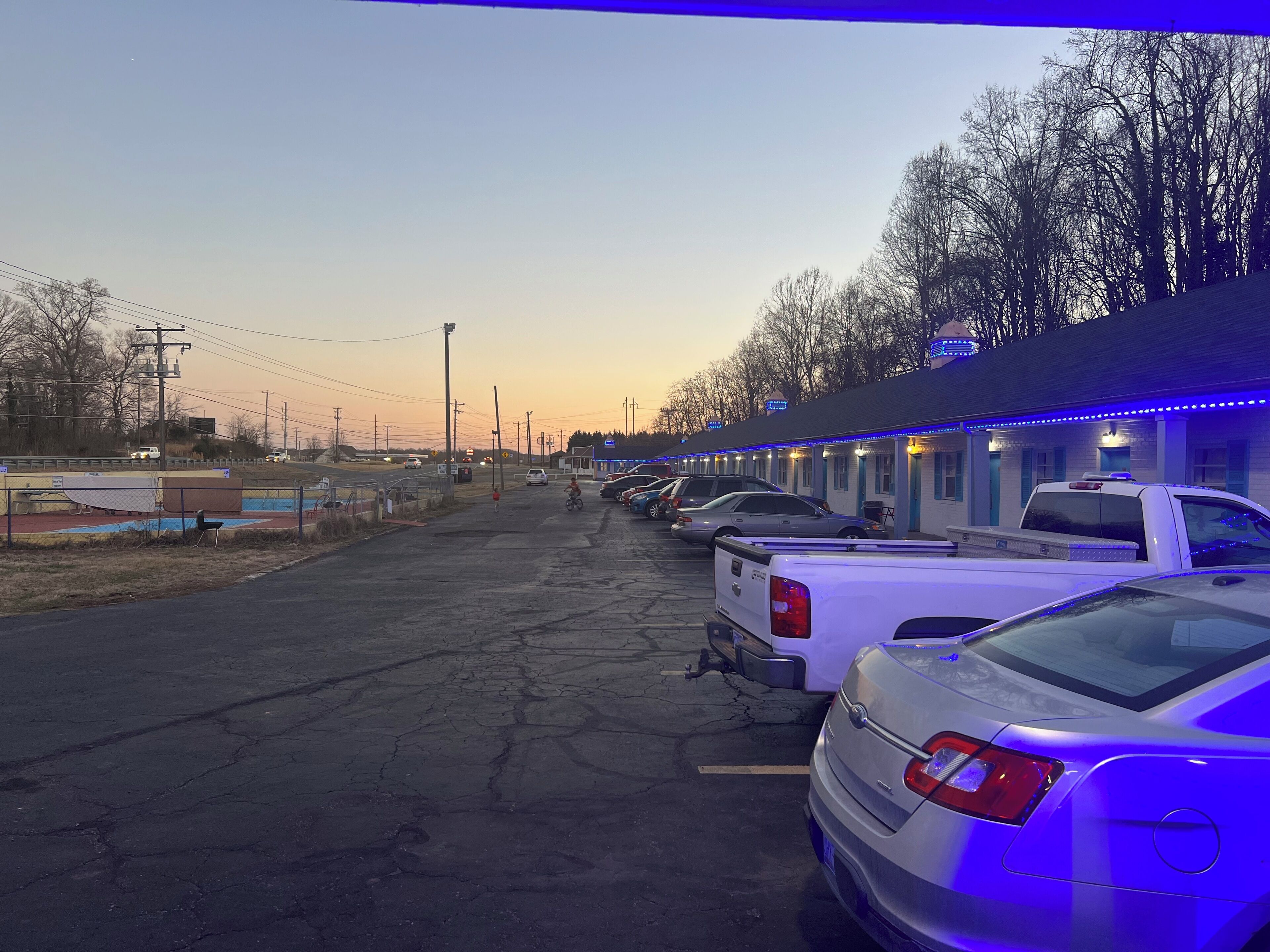 A row of motel rooms with a parking lot in front.