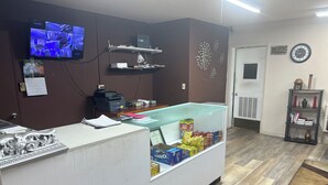 Zona de recepción con mostrador, computadora y vitrina de vidrio con aperitivos.