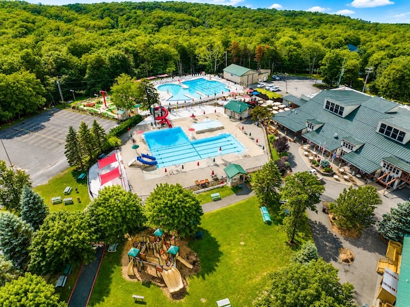 Vue aérienne d’un complexe hôtelier doté de plusieurs piscines, d’une aire de jeux et d’un bâtiment surmonté d’un toit végétalisé.