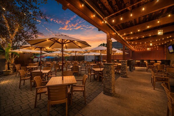 Une terrasse extérieure avec des tables et des chaises, protégée par des parasols et illuminée de guirlandes lumineuses.
