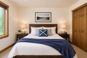 A bedroom with a bed, two bedside tables, a nightstand, a window, a door, and a framed picture on the wall.
