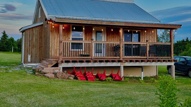 A wooden cabin with a porch, large windows, and a metal roof. - Prince Edward Island 2 bedroom waterfront cottage in South Rustico (New Glasgow)