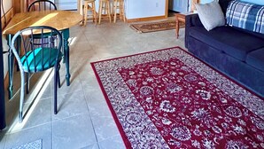A spacious living area with a dining table, a sofa, and a red patterned rug. - Prince Edward Island 2 bedroom waterfront cottage in South Rustico (New Glasgow)