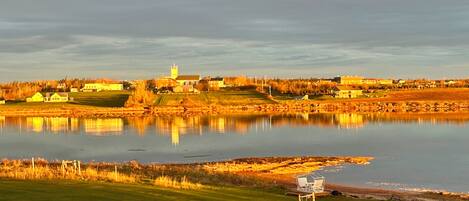 A lakeside view with a church, houses, and a grassy area with a bench.