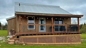 A wooden building with a metal roof, a porch with railings, and a fenced area. - Prince Edward Island 2 bedroom waterfront cottage in South Rustico (New Glasgow)