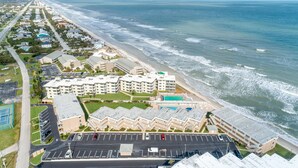 An aerial view of a coastal hotel with multiple buildings, a parking lot, and a beach.