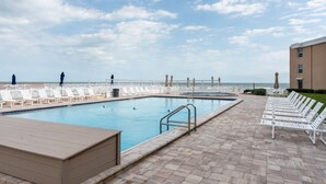 A pool area with lounge chairs and a view of the ocean.
