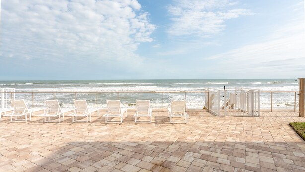 A beachside patio with white lounge chairs and a view of the ocean.