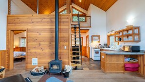 A cozy cabin interior with a wood-burning stove, a loft bedroom, a kitchen area, and a dining space. - Jenny Creek Cabin w/ Jacuzzi and Wood Stove at Green Springs Inn (Ashland)