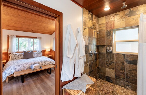 Une chambre avec un plafond en bois et un grand lit, une douche aux carreaux de pierre et une fenêtre avec des rideaux.