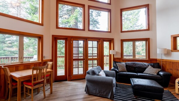 A spacious room with a wooden dining table, chairs, a black leather sofa, and a large window overlooking a deck. - Jenny Creek Cabin w/ Jacuzzi and Wood Stove at Green Springs Inn (Ashland)