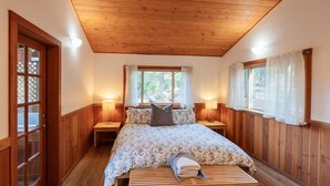 A bedroom with a wooden ceiling, a bed with a floral bedspread, two bedside lamps, and a window with curtains. - Jenny Creek Cabin w/ Jacuzzi and Wood Stove at Green Springs Inn (Ashland)