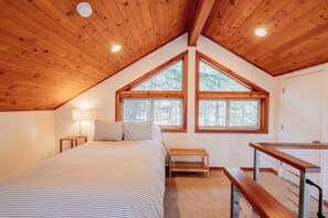 A bedroom with a sloped ceiling, large windows, a bed, a bedside table with a lamp, a bench, and a desk with a chair. - Jenny Creek Cabin w/ Jacuzzi and Wood Stove at Green Springs Inn (Ashland)