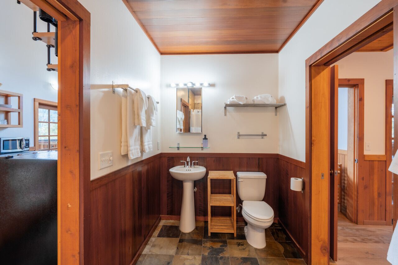 A bathroom with a wooden vanity, a pedestal sink, a toilet, and a mirror with lights.