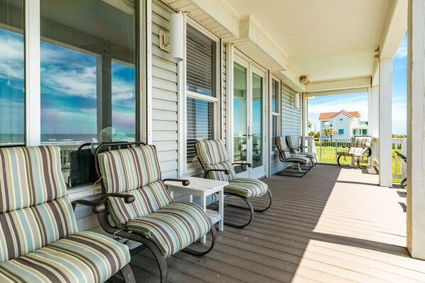 Eine überdachte Veranda mit gestreiften Stühlen und einem Tisch mit Blick auf eine Wohngegend.