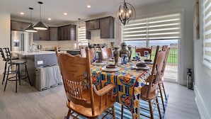 Una cocina moderna con comedor, que incluye una isla grande, luces colgantes y vistas al exterior.