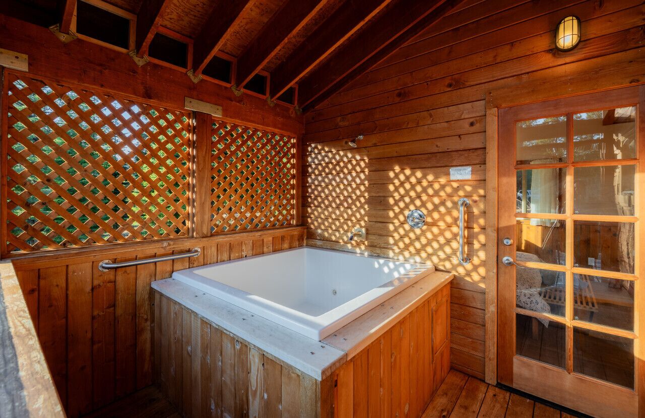 A wooden cabin with a wooden bathtub, a glass door, and a lattice window.