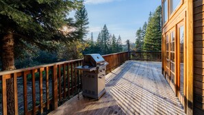 A wooden deck with a grill, surrounded by tall trees and a wooden building.