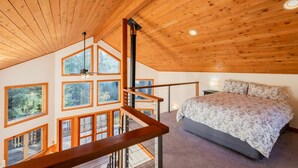 A bedroom with a large bed, wooden ceiling, and multiple windows.