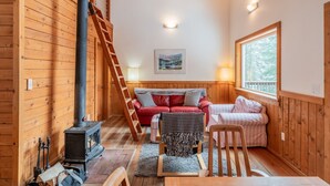A cozy cabin interior with a wooden interior, a fireplace, a red sofa, and a window providing natural light. - Hobart Peak Cabin w/ Jacuzzi and Wood Stove at Green Springs Inn (Ashland)