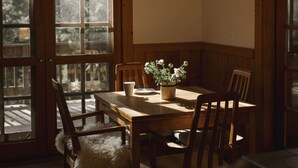 A dining area with a wooden table, four chairs, a vase with flowers, and a window with frosted glass panels. - Hobart Peak Cabin w/ Jacuzzi and Wood Stove at Green Springs Inn (Ashland)