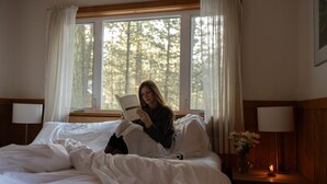 A room with a bed, a bedside lamp, a nightstand with a vase of flowers, and a window with curtains. - Hobart Peak Cabin w/ Jacuzzi and Wood Stove at Green Springs Inn (Ashland)