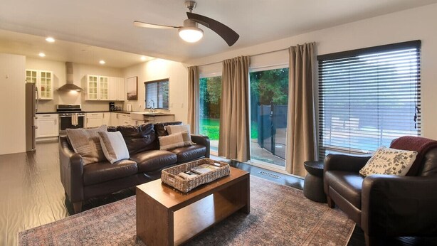 A modern living room with a leather sofa, a coffee table, and a large window with blinds. - The Charming Home with a Pool (Yuba City)