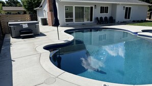 A swimming pool with a curved edge, a covered hot tub, and a patio area with outdoor furniture. - The Charming Home with a Pool (Yuba City)