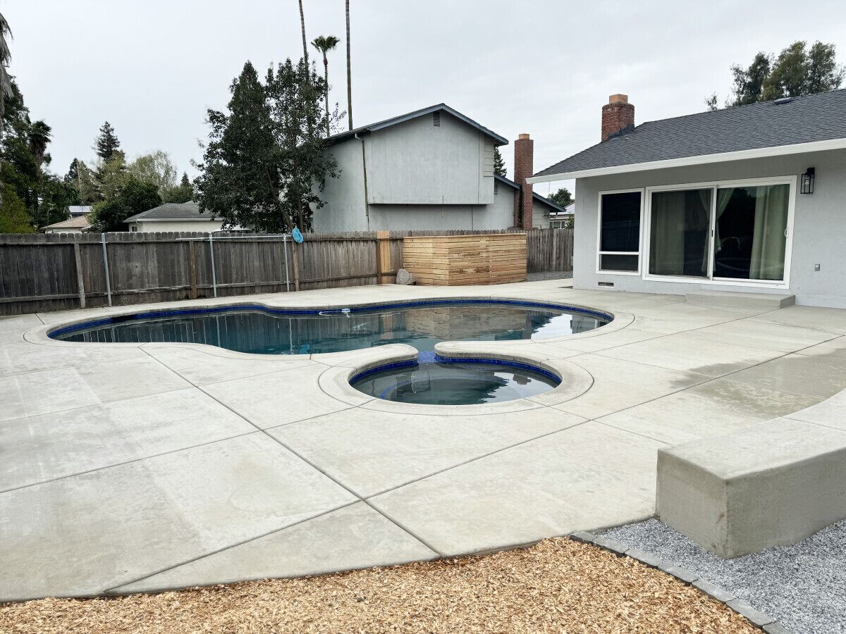 A backyard with a swimming pool, a wooden fence, and a house with a chimney.