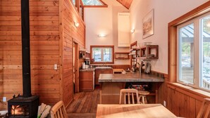 A cozy cabin interior with a wood stove, wooden walls, a kitchen area, and a dining table. - Chinquapin Mountain Cabin w/ Jacuzzi and Wood Stove at Green Springs Inn (Ashland)