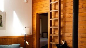 A cozy room with a blue sofa, a small table, a wooden ladder, and a wood-burning stove. - Chinquapin Mountain Cabin w/ Jacuzzi and Wood Stove at Green Springs Inn (Ashland)