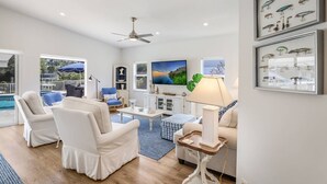 A spacious living room with a pool view, white furniture, and a ceiling fan. - Dock Holiday: On Canal, Pool & Spa by Anna Maria Life Vacation Rentals (Anna Maria)