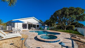 A backyard with a swimming pool, lounge chairs, and a covered patio area. - Dock Holiday: On Canal, Pool & Spa by Anna Maria Life Vacation Rentals (Anna Maria)