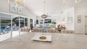 A spacious living area with a marble dining table, comfortable seating, and a view of an outdoor pool. - Dock Holiday: On Canal, Pool & Spa by Anna Maria Life Vacation Rentals (Anna Maria)