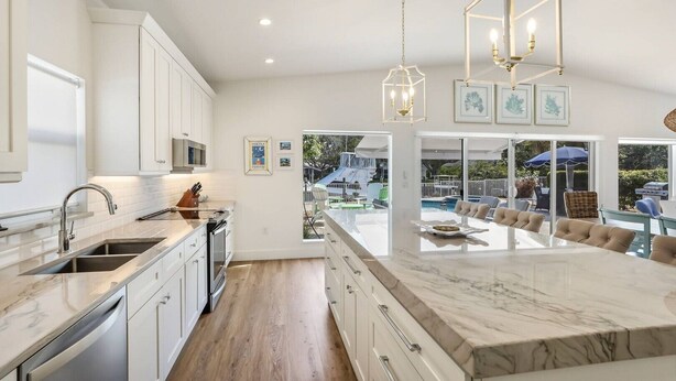 A modern kitchen with white cabinetry, a marble island, and pendant lighting. - Dock Holiday: On Canal, Pool & Spa by Anna Maria Life Vacation Rentals (Anna Maria)