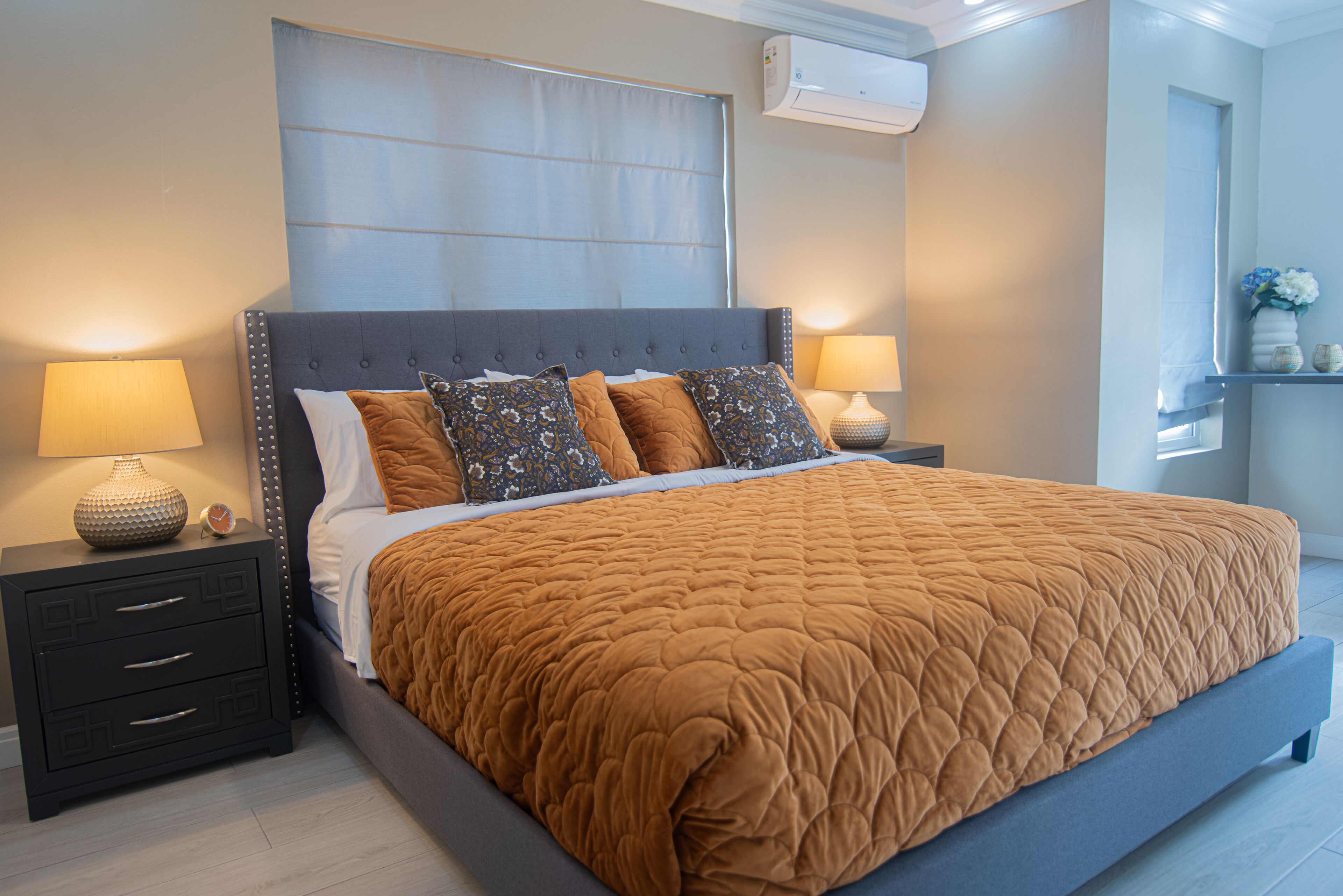 A neatly made bed with a brown quilt, two bedside tables with lamps, and a window with a curtain.
