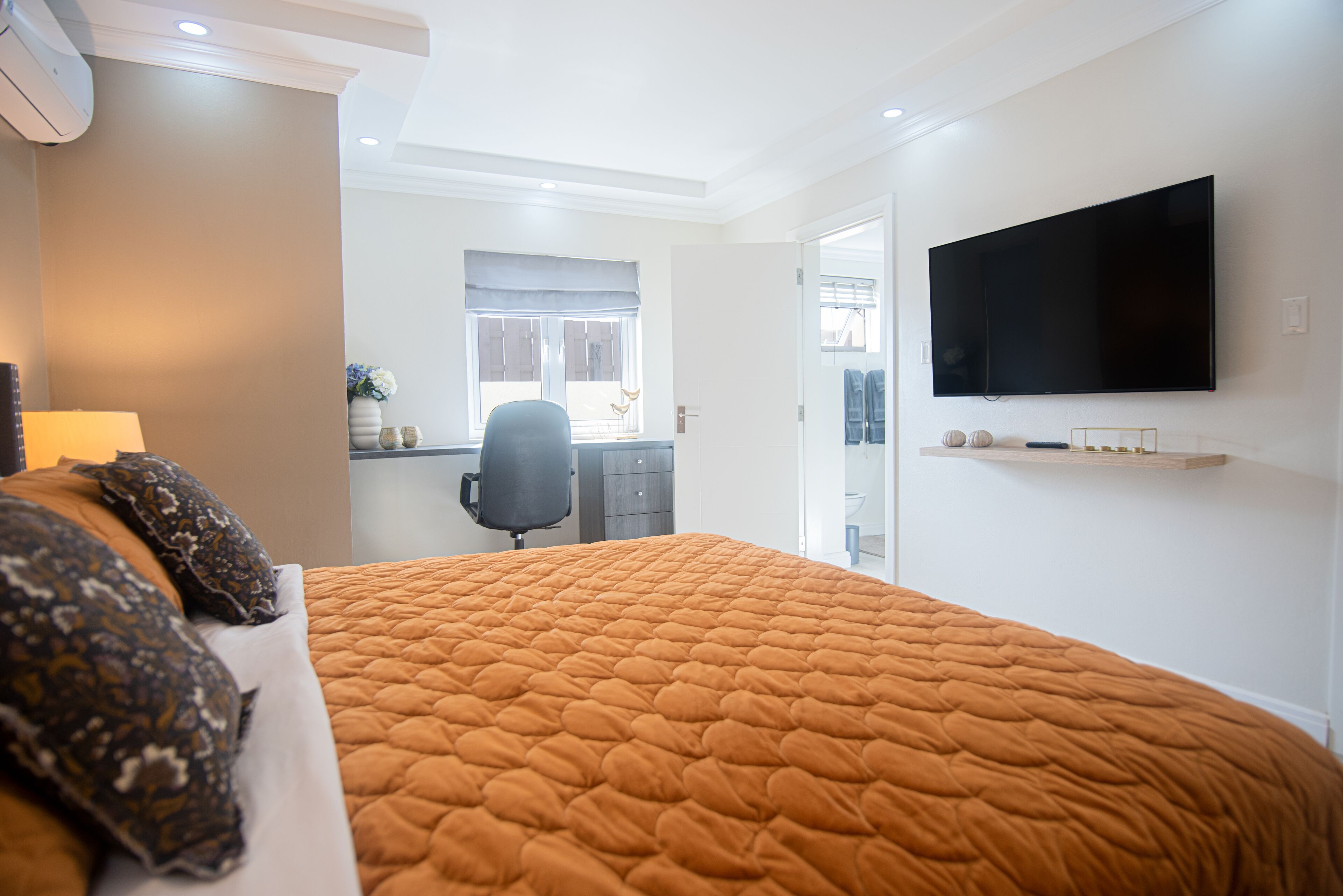 A bedroom with a large bed, a flat-screen TV mounted on the wall, and a desk with a chair.