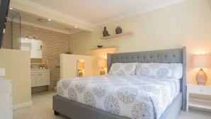 Une chambre avec un grand lit, une table de chevet, une commode, un miroir, une armoire et une salle de bain avec un lavabo et un miroir.