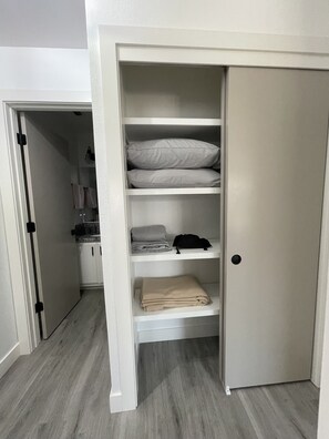 Un dressing ouvert avec des étagères où sont pliés des vêtements, un sac suspendu et une porte.