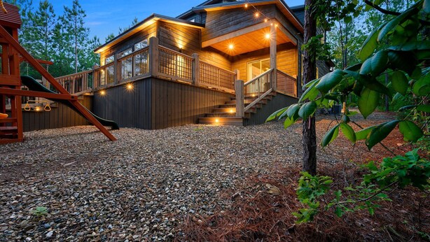 Une cabane en bois avec un escalier menant à une terrasse, entourée d’arbres et de gravier.